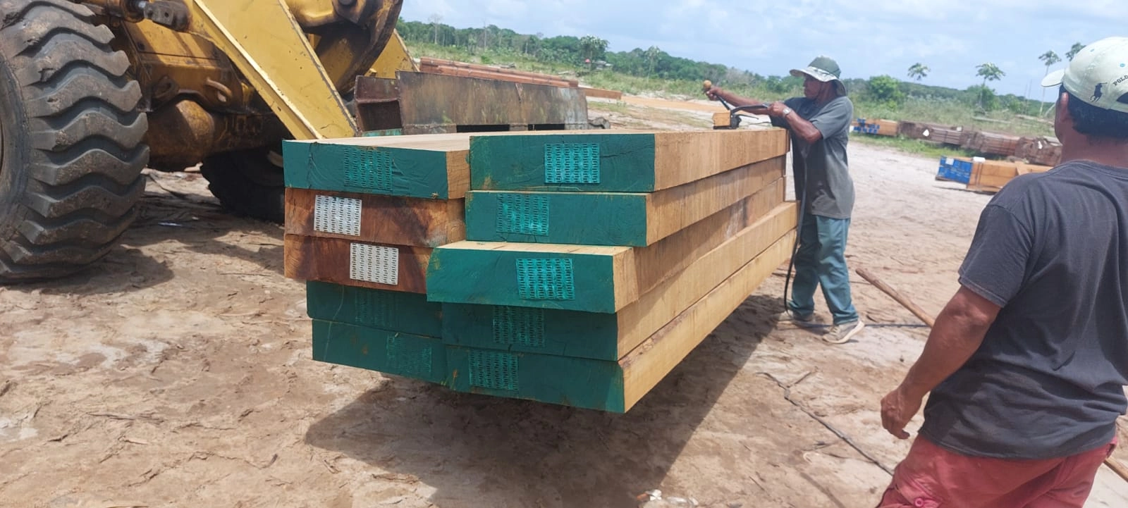 Crew guiding a loader carrying teal-ended hardwood squares